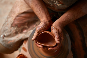 Close-up hands of a male potter in apron molds bowl from clay, selective focus
