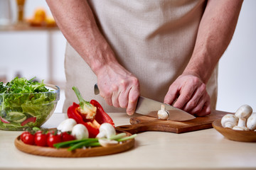 Man cooking at kitchen making healthy vegetable salad, close-up, selective focus.