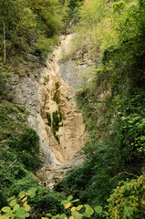 Seasonal waterfall on exposed outcrop in woods near Quinten, Swiss Alps