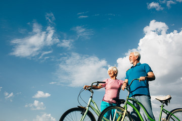 Senior couple with their bicycles standing against the blue sky, and look away , side view
