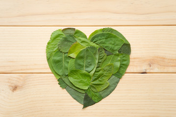Corazón hecho con trozos de hojas verdes sobre una superficie de madera. Concepto: protección del medio ambiente.