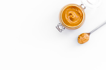 Nut butter, peanut butter in glass jar and spoon with butter on white background top view copy space