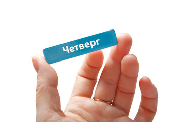 The hand holds a miniature card with the inscription Thursday in Russian. Isolated on white background.