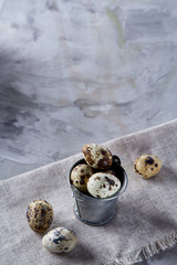 Small decorative bucket filled with quail eggs on napkin over white textured background, close-up, selective focus.