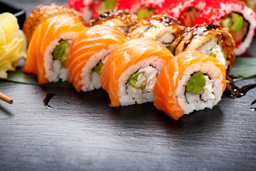 Sushi rolls closeup. Japanese food in restaurant. Roll with salmon, eel, vegetables and flying fish caviar on black slate background