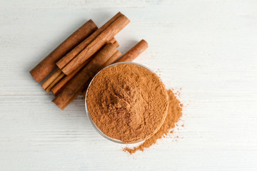 Bowl with aromatic cinnamon powder and sticks on wooden background