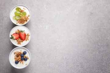 Bowls with yogurt, granola and different fruits on gray background, top view