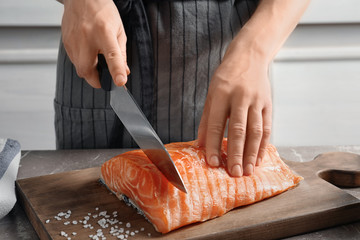 Woman cutting raw salmon fillet on wooden board