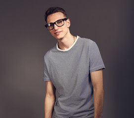 Fashion smiling man posing in trendy glasses in strip casual shirt and white jeans on grey background. Toned closeup portrait with empty copy space