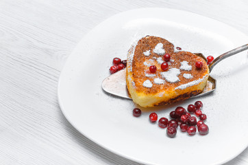 Freshly baked heart shape curd on the plate with cranberry and powdered sugar on white wooden table background.