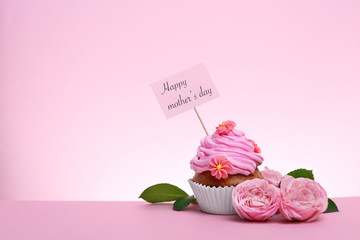 Tasty cupcake and flowers for Mother's Day on color background