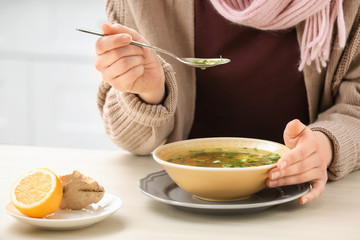 Sick young woman eating broth to cure cold at table in kitchen