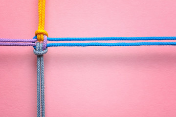 Different ropes tied together with knot on color background. Unity concept - obrazy, fototapety, plakaty