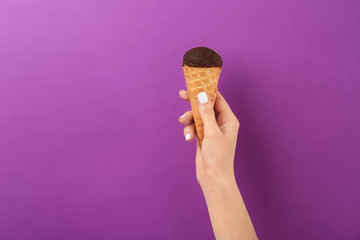 Woman holding yummy ice cream on color background. Focus on hand