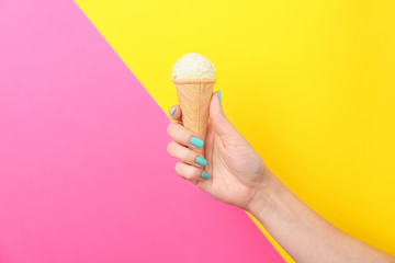 Woman holding yummy ice cream on color background. Focus on hand