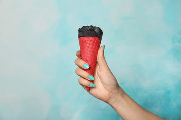 Woman holding yummy ice cream on color background. Focus on hand