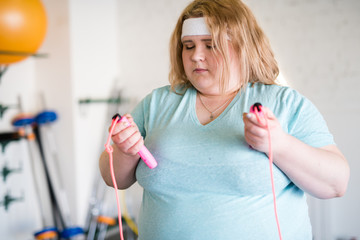 Waist up portrait of  obese young woman holding jumping rope during weightloss training in gym,...