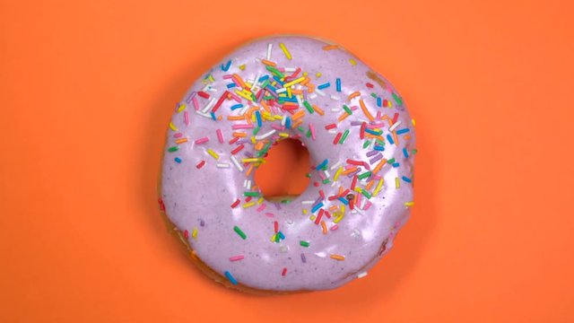 Bright and colorful sprinkles donut close-up, macro shot, fast spinning on a orange background.