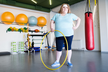 Full length portrait of  obese young woman posing with hula hoop  during weightloss training in gym, copy space © Seventyfour