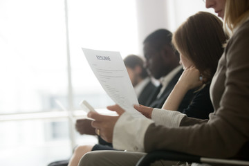 Multiracial business people waiting in queue preparing for job interview concept, diverse unemployed vacancy applicants holding reading cvs getting ready, human resources concept, focus on resume