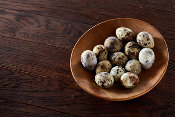 Fresh quail eggs in a wooden bowl on a dark wooden background, top view, close-up