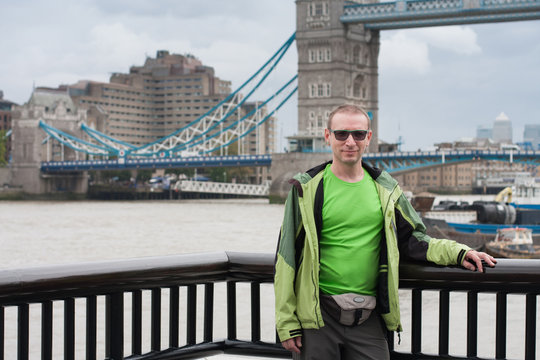 Caucasian man is standing on embankment of river Thames, on background Tower Bridge.