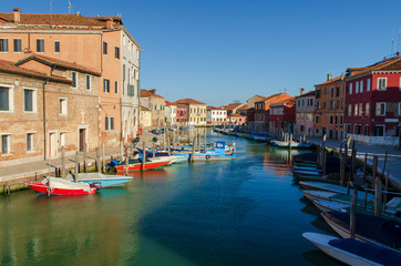 Large venetian canal with boats docked and colorful houses on the Murano island