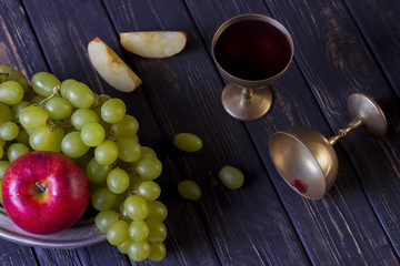 Copper glass with wine grapes and apples on dark wooden background.