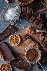 Dark chocolate bars with dry orange slices, cinnamon sticks and salt on blue background.