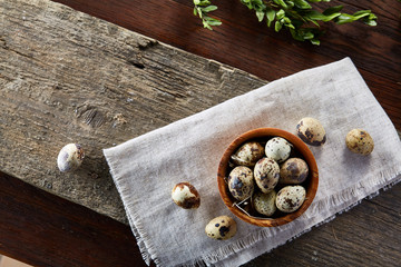 Rural still life with bowl full of eggs quail, eggs on a homespun napkin, boxwood on wooden background, top view