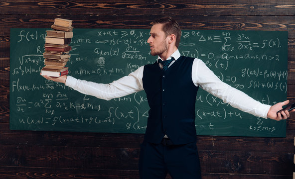 Balance between technology and knowledge. Blond guy in suit holding a pile of books in one hand and a smartphone in another