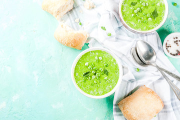 Green pea soup with fresh bread on light blue concrete table, copy space top view