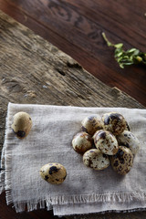 Quail eggs arranged in pyramid on a napkin with boxwood branches over a wooden table, close-up, selective focus.