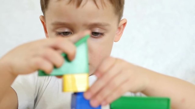 Child boy playing with colored blocks, in slow motion. The camera moves from the child's face to the toys