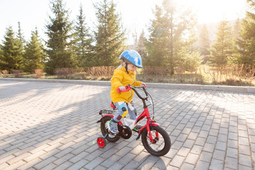 Three years old child boy in safety helmet riding on a bicycle at cobbles road in the city park in spring or summer. Happy childhood and kids first trip on a four-wheeled bicycle