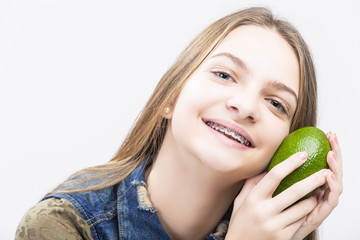 Portrait of Smiling Caucasian Female Teenager With Teeth Braces. Posing with Long Green Avocado Fruit.