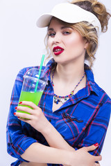 Passionate Sexy Caucasian Blond Woman in Checked Shirt. Drinking Green Juice Through Straw. Posing in Sun Visor Against White.