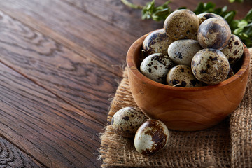 Rural still life with bowl full of eggs quail, eggs on a homespun napkin, boxwood on wooden background, top view
