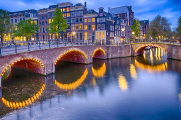 Fototapeta na wymiar Travel Concepts. Night View of Amterdam Cityscape with One of Its Canals. Illuminated Bridge and Traditional Dutch Houses At Twilight.