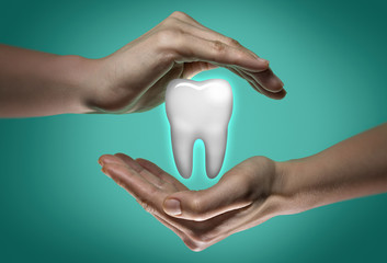 A tooth between two palms of a woman on  blue and green background. Dental care concept.