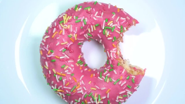 Somebody bit a glazed sprinkles donut. Yummy slowly spinning on a rotating table.