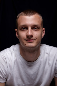 Handsome young caucasian man. In white t-shirt. Smile.Emotion. On black background.Portrait