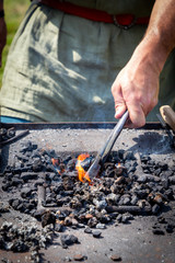 A blacksmith heats the iron in the embers