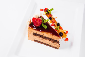 a piece of cake with chocolate decorated with strawberries and mint leaves (on white background)