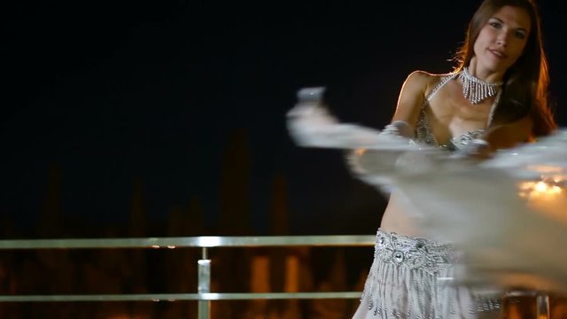 Beautiful young woman in oriental ethnic costume dances at night outdoor