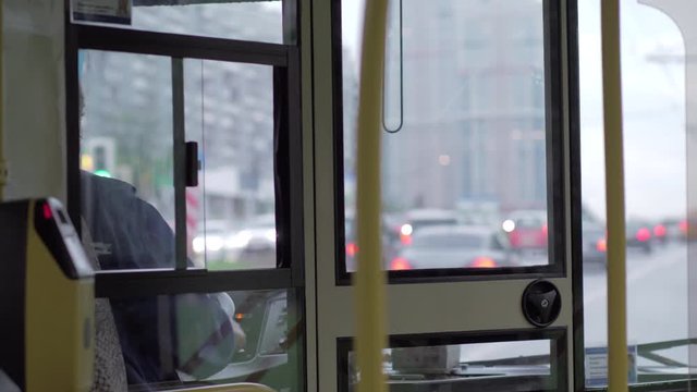 View to the road traffic through the bus cabin with unidentified woman driver at the wheel. Traveling by public transport in the city