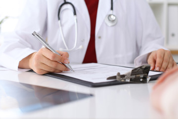Fototapeta premium Close up of a female doctor filling up an application form while consulting patient