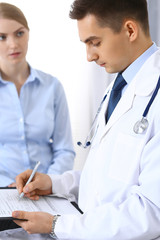 Male doctor holding application form while consulting female patient in hospital office. Perfect service in medicine and healthcare concept