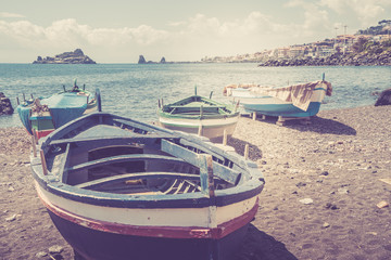 Fishing boats on the beach of Capomulini with a view of the Acitrezza stacks. Vintage filtered image