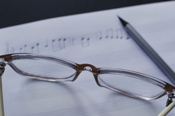 Close-up view of the pencil, eyeglasses laying on the sheet notes with handwritten notes. The concept of the music creating, composing, note writing, music art.
